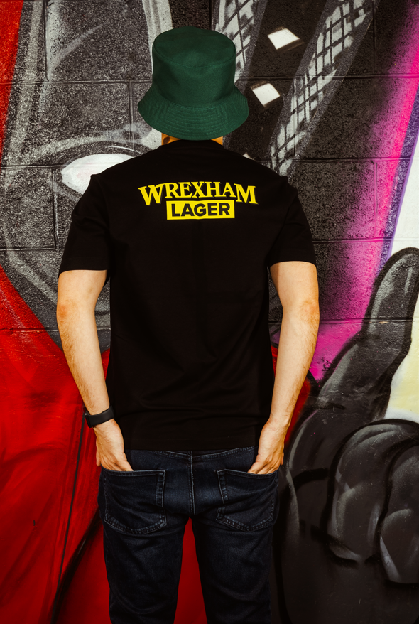 Person wearing a black t-shirt with 'Wrexham Lager' text against a colorful graffiti wall.
