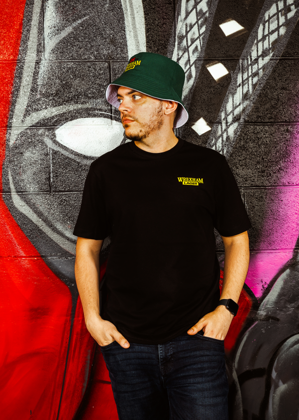 Person wearing a black t-shirt with text and a green cap in front of a colorful mural.