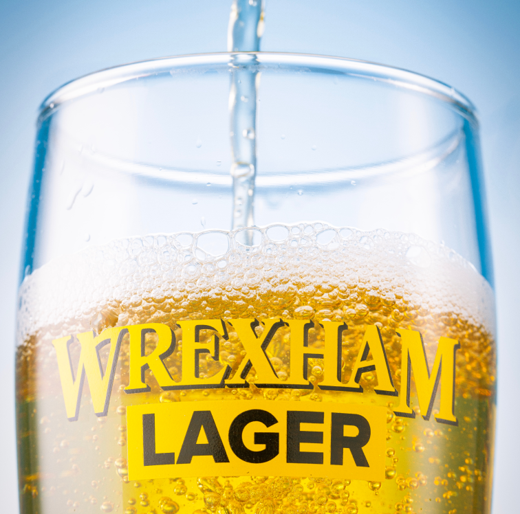 Wrexham Lager being poured into a glass with a blue background