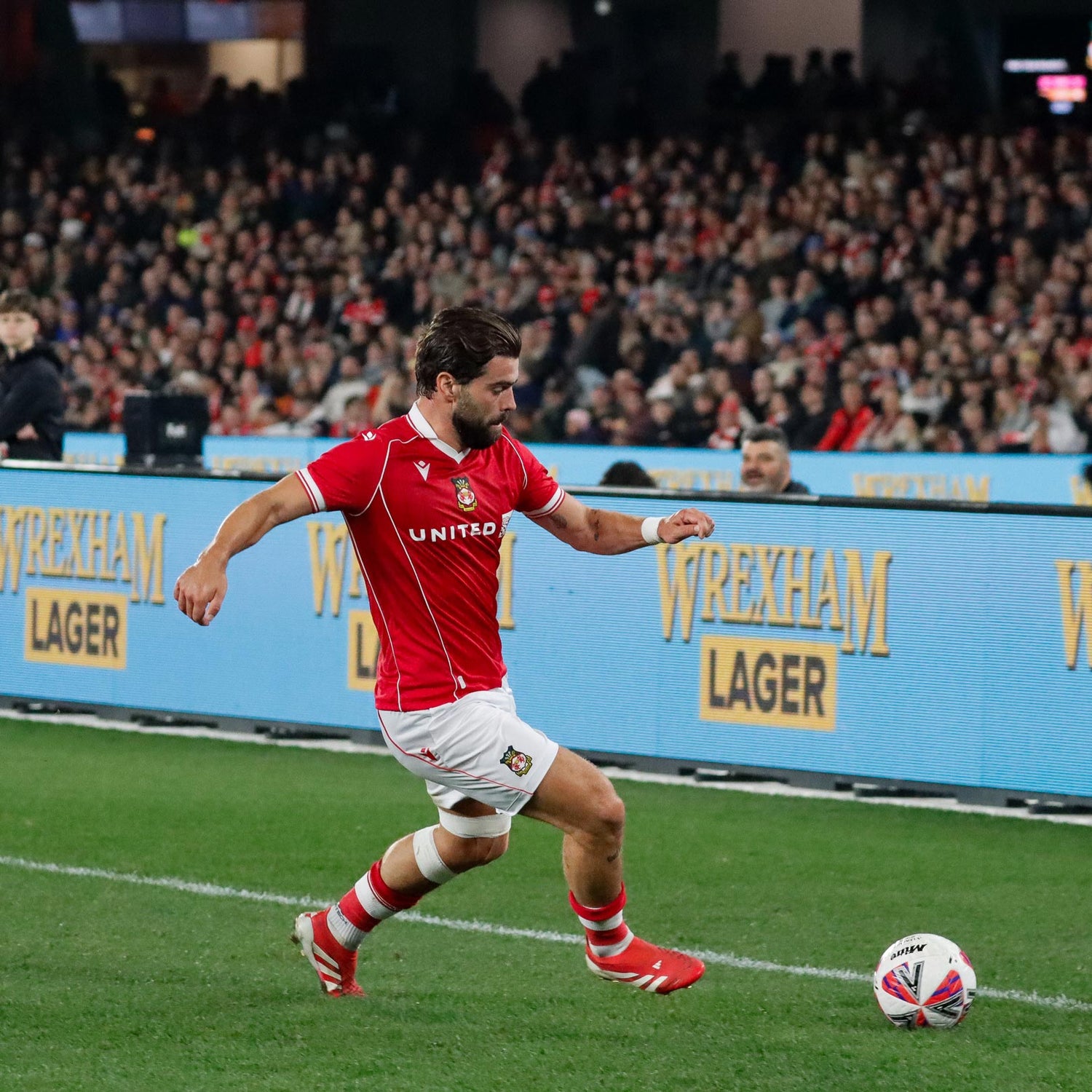 Elliot Lee on the field with Wrexham Lager advertising in the background.