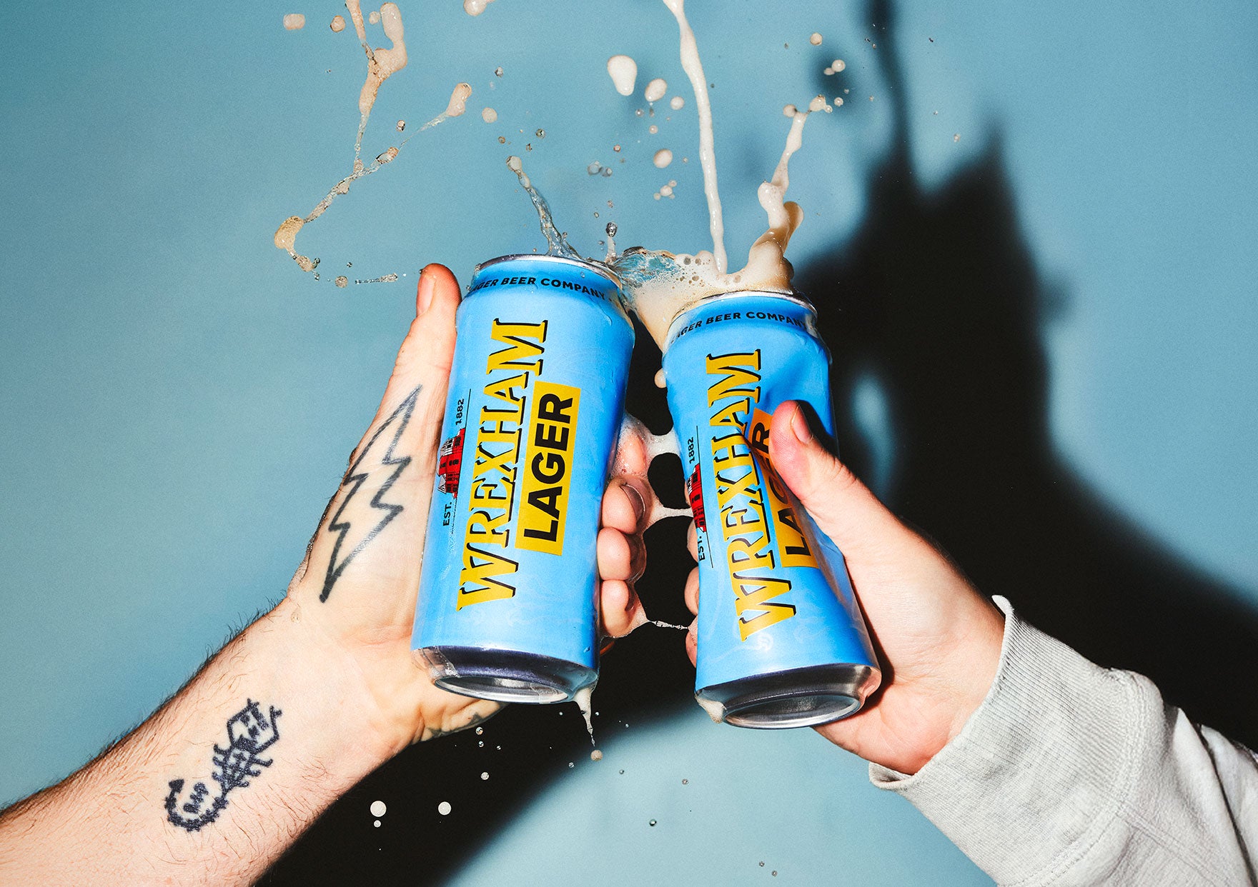 Two cans of Wrexham Lager being held up against a blue background