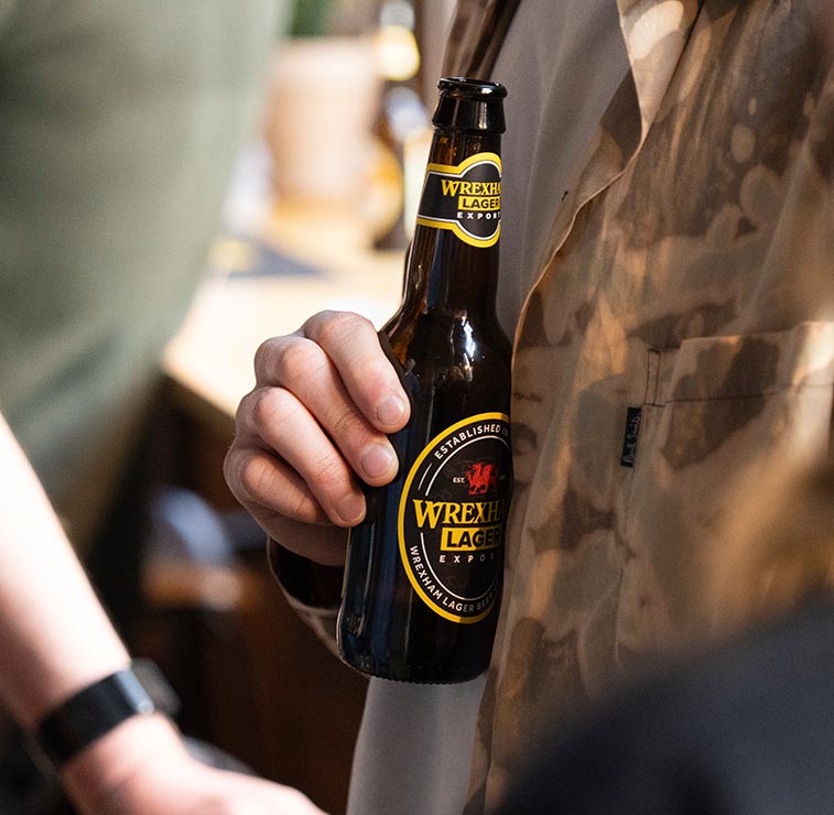 Person holding a bottle of Wrexham Lager in a casual setting