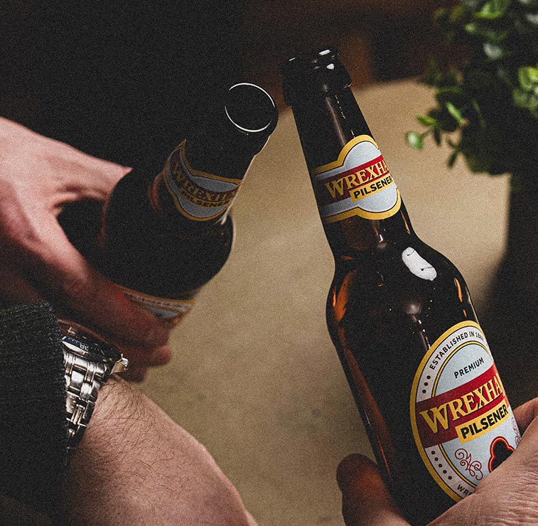 Two bottles of Wrexham Pilsener beer being held together.