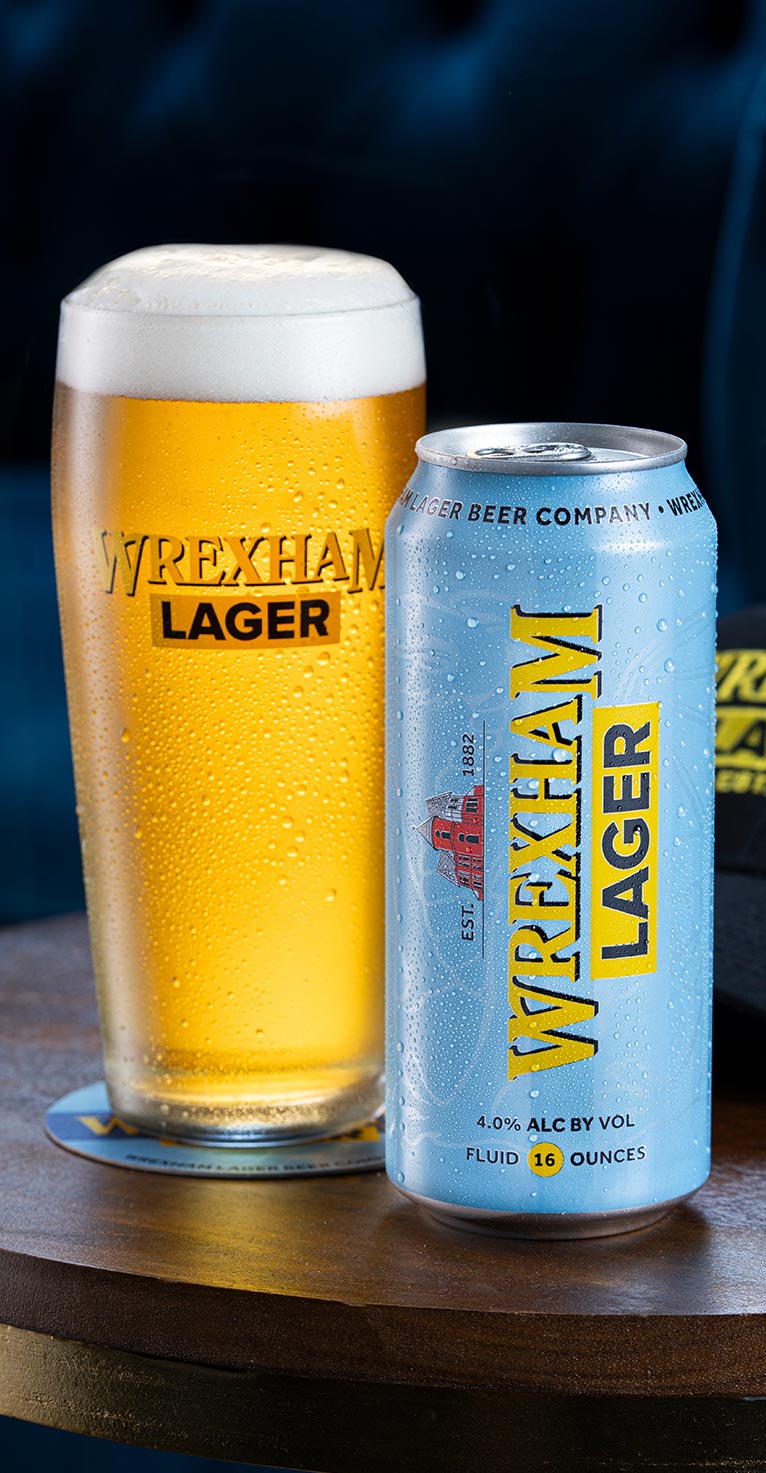 A pint of Wrexham Lager and can on a wooden surface with a dark background