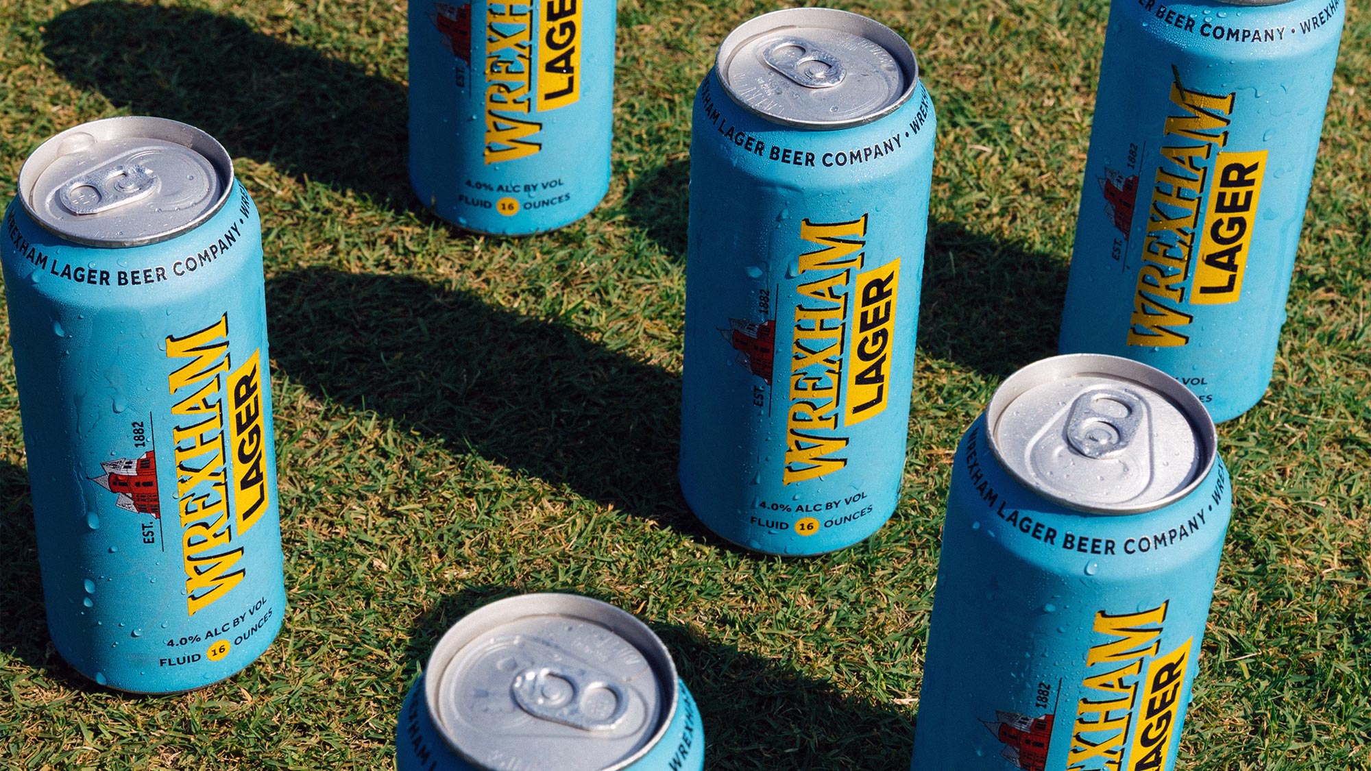 Multiple cans of Wrexham Lager arranged on a soccer pitch.