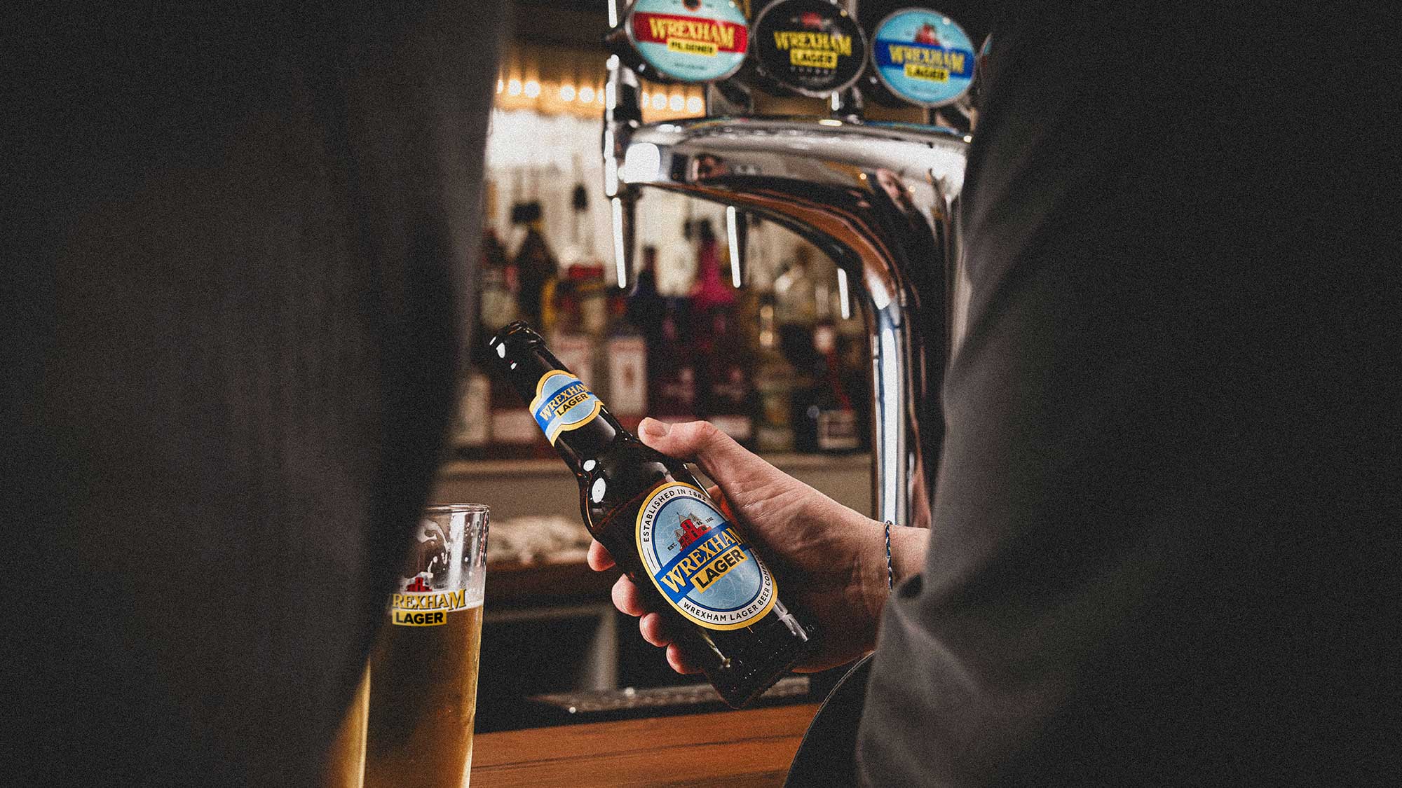 A man at a bar drinking Wrexham Lager